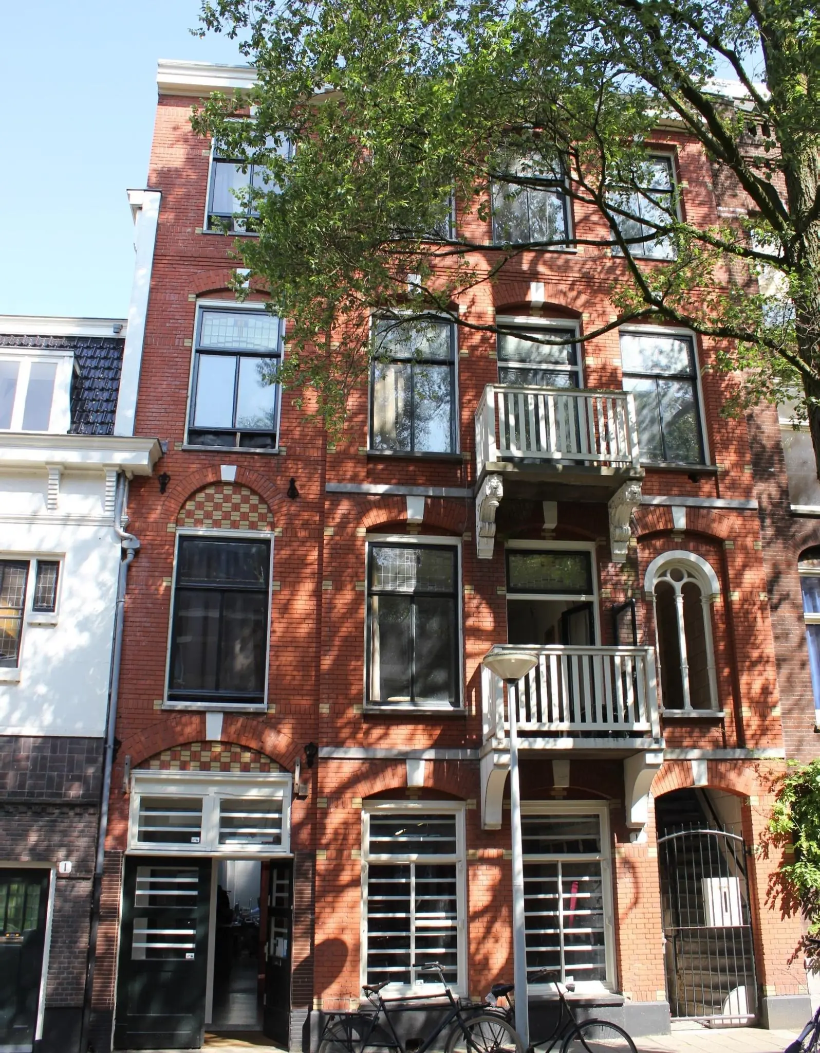 Voorgevel van een klassiek rood bakstenen woonhuis aan de Graaf Florisstraat met hoge ramen, twee balkons en fietsen voor de deur.